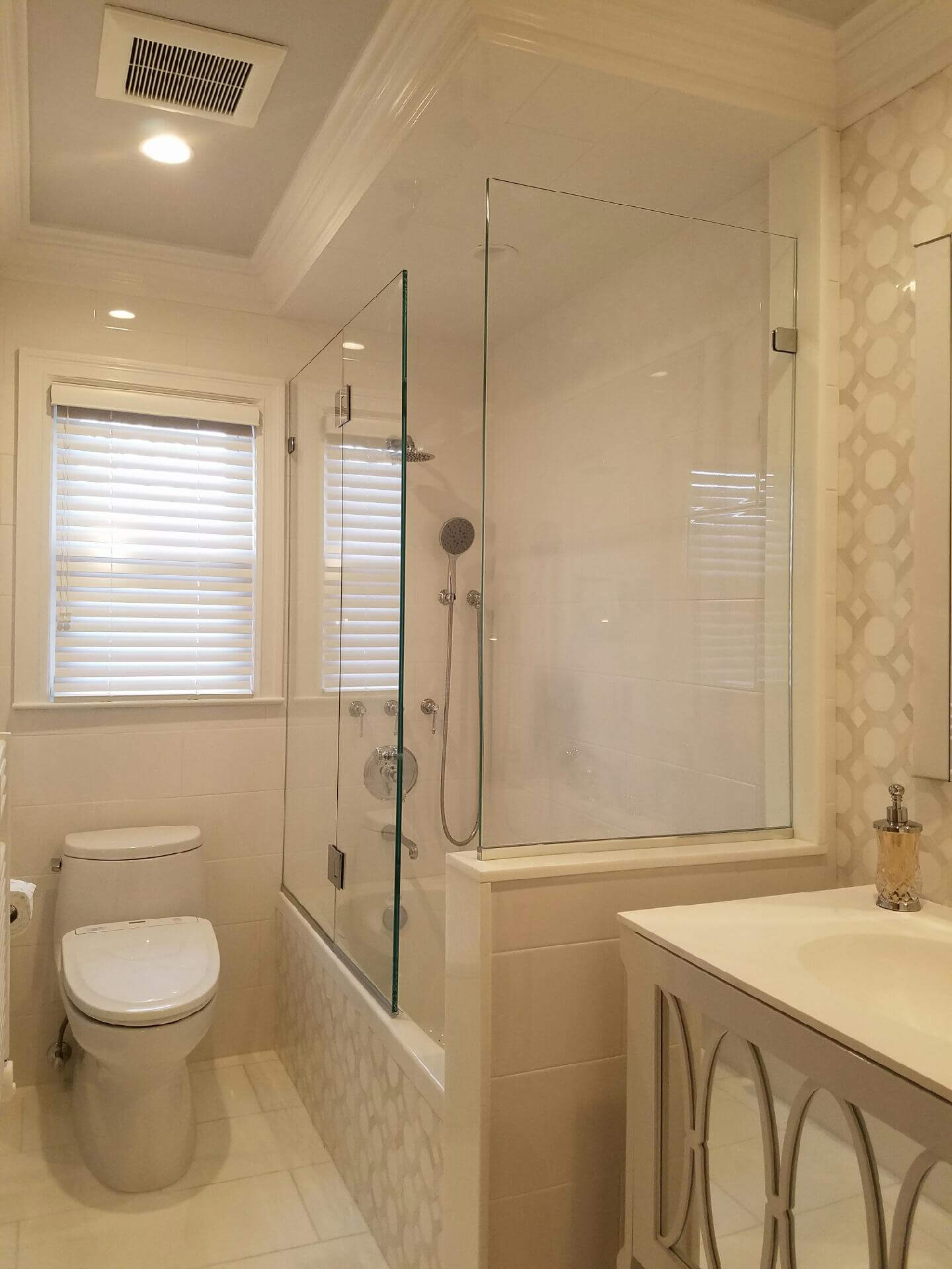 frameless glass shower with white toilet, bath, and window with blinds closed