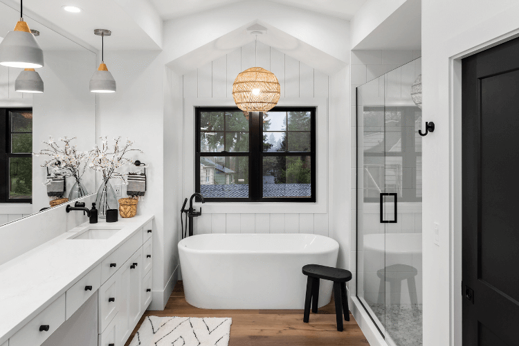Remodeled white bathroom with a freestanding soaking tub, glass-enclosed shower, and wood flooring