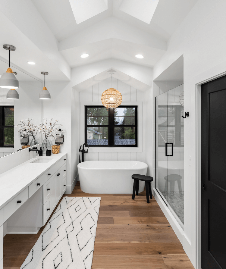 Remodeled white bathroom with a freestanding soaking tub, glass-enclosed shower, and wood flooring